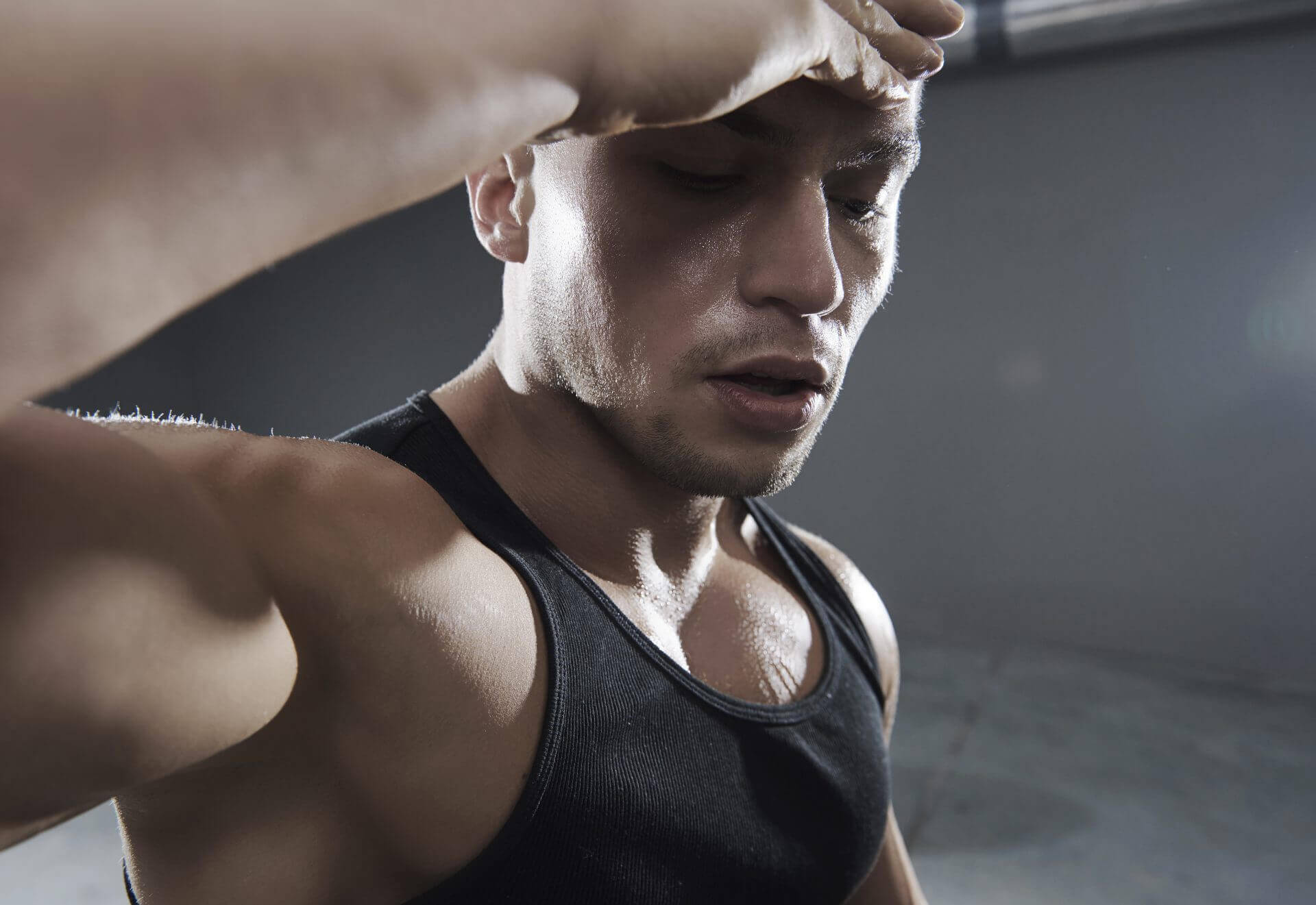 Young man in a black vest wiping sweat from his forehead.