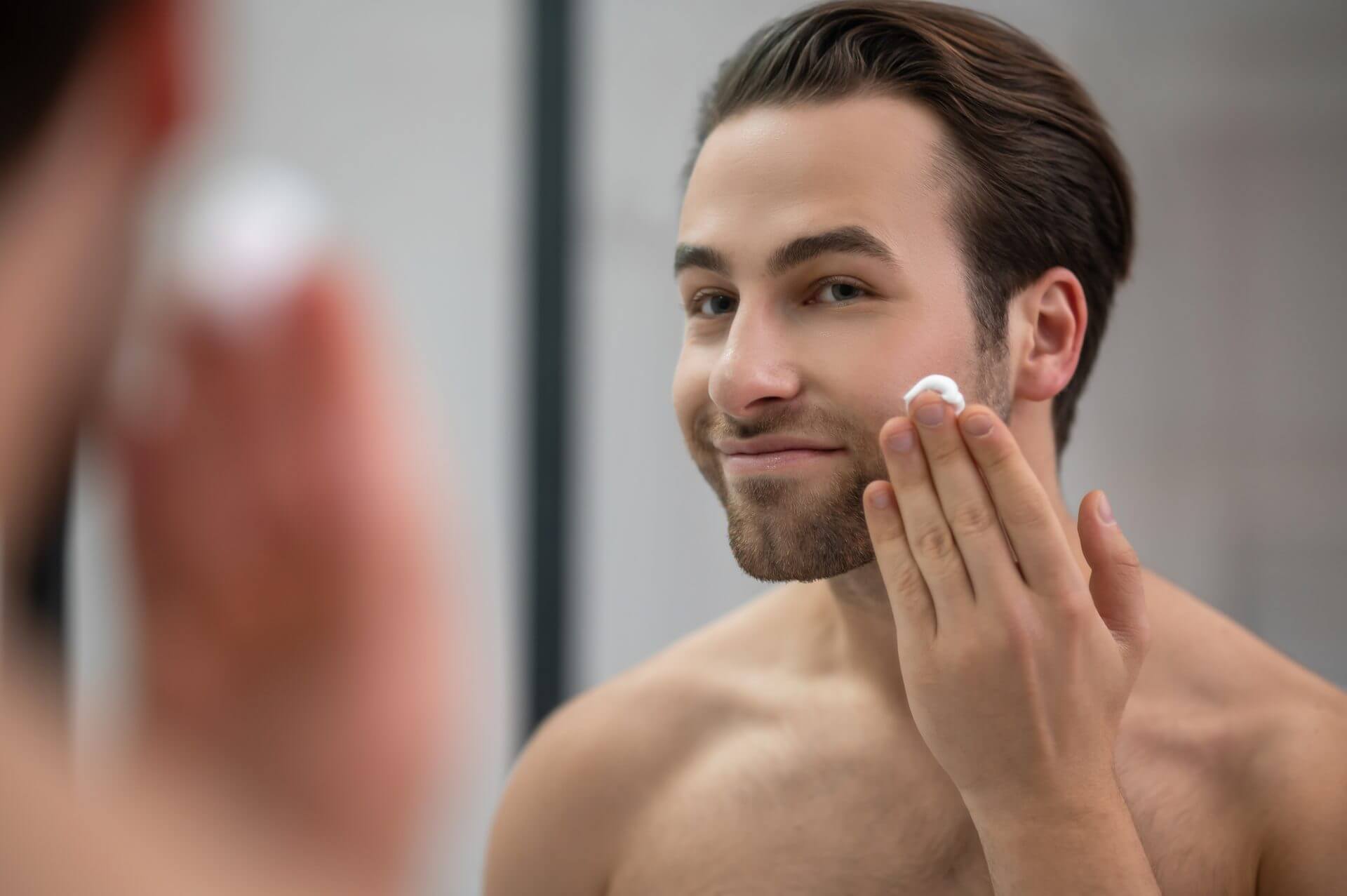 man standing near mirror applying skincare cream to his face